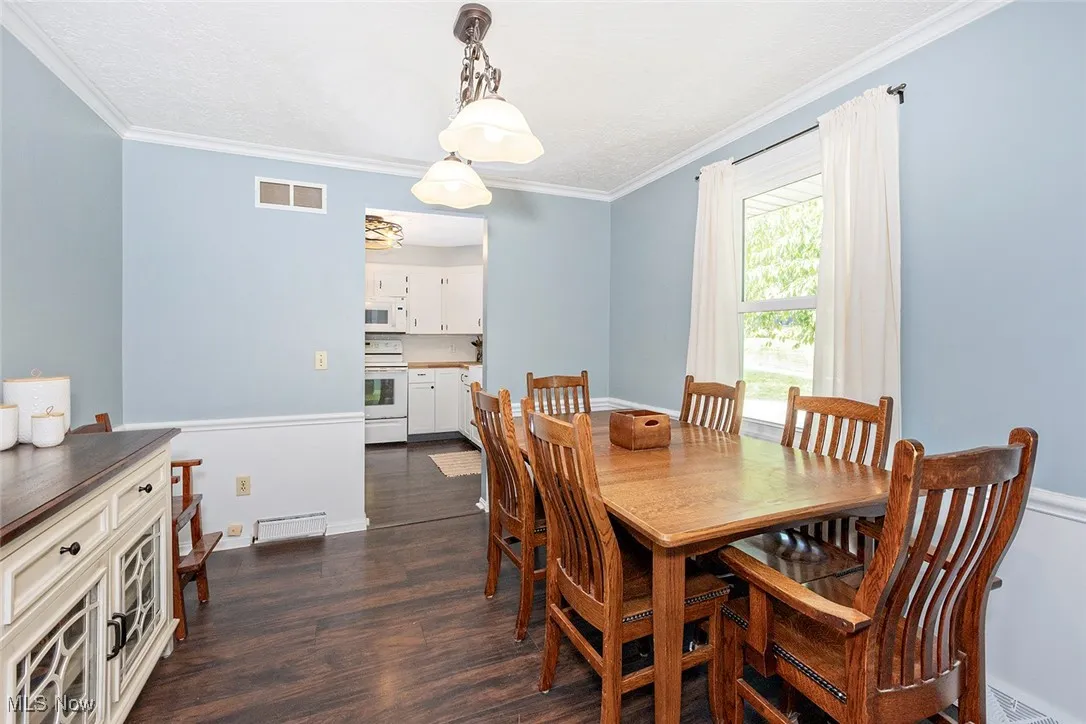 Dining area featuring dark wood-type flooring, ornamental molding, and a textured ceiling