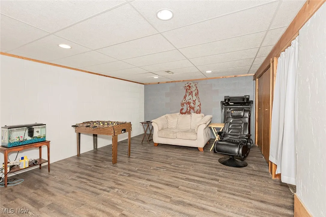 Living area with a drop ceiling, recessed lighting, concrete block wall, and wood finished floors