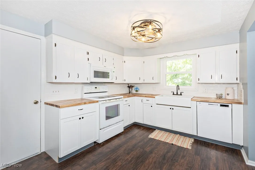 Kitchen with butcher block countertops, white appliances, dark wood finished floors, and a textured ceiling