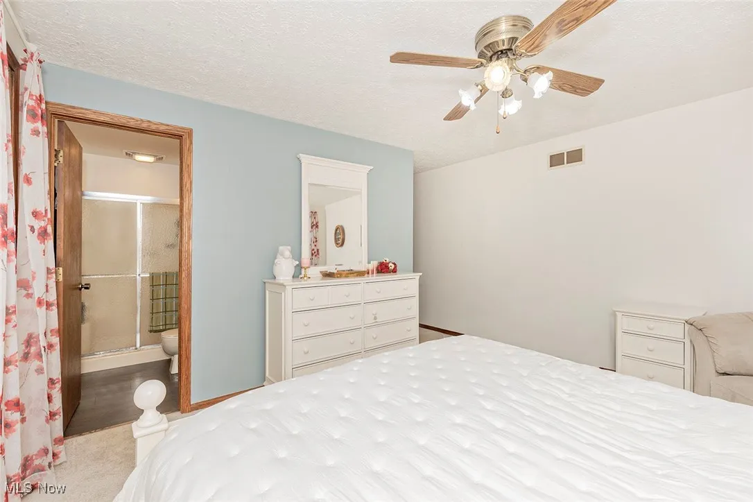 Bedroom with a textured ceiling, carpet, ceiling fan, and ensuite bathroom