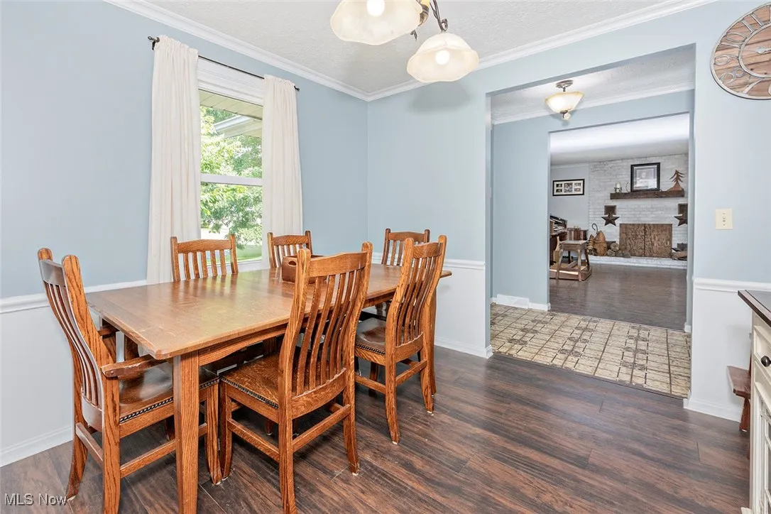 Dining space featuring wood finished floors, crown molding, a brick fireplace, and a textured ceiling