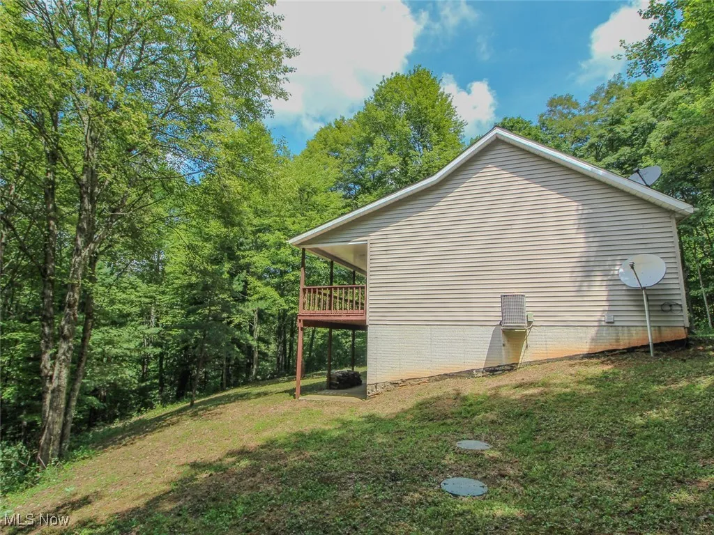 View of property exterior with a yard, a wooden deck, and a wooded view