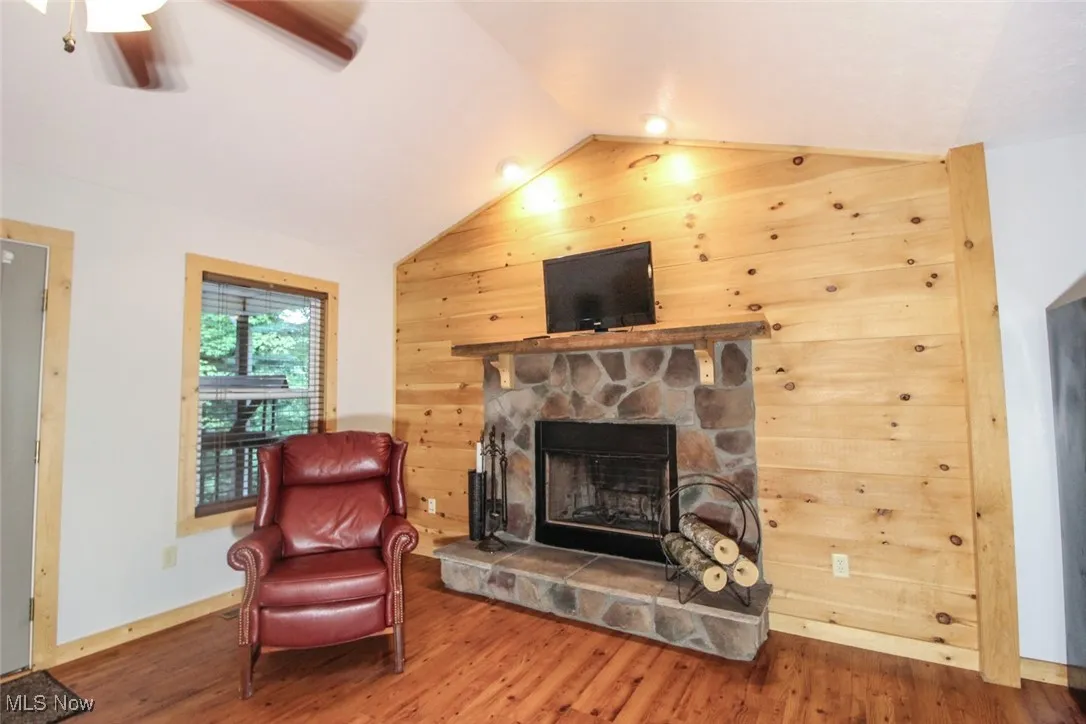 Living area featuring vaulted ceiling, wooden walls, wood finished floors, a fireplace, and a ceiling fan