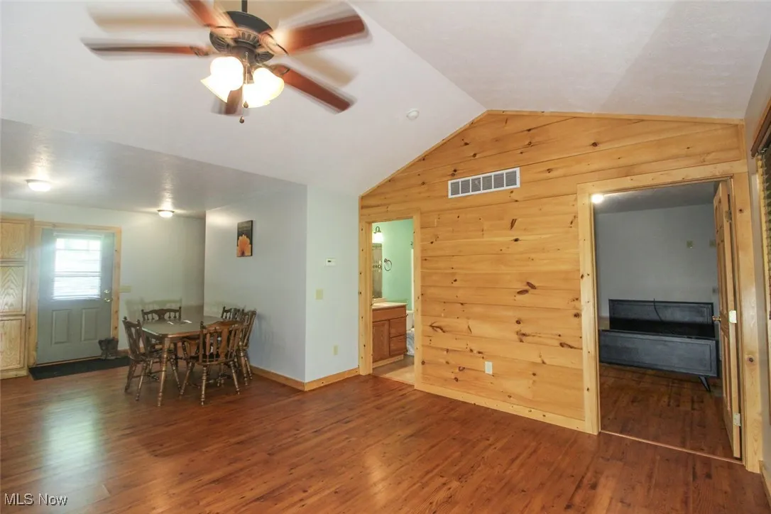 Dining area featuring wooden walls, lofted ceiling, a ceiling fan, and wood finished floors