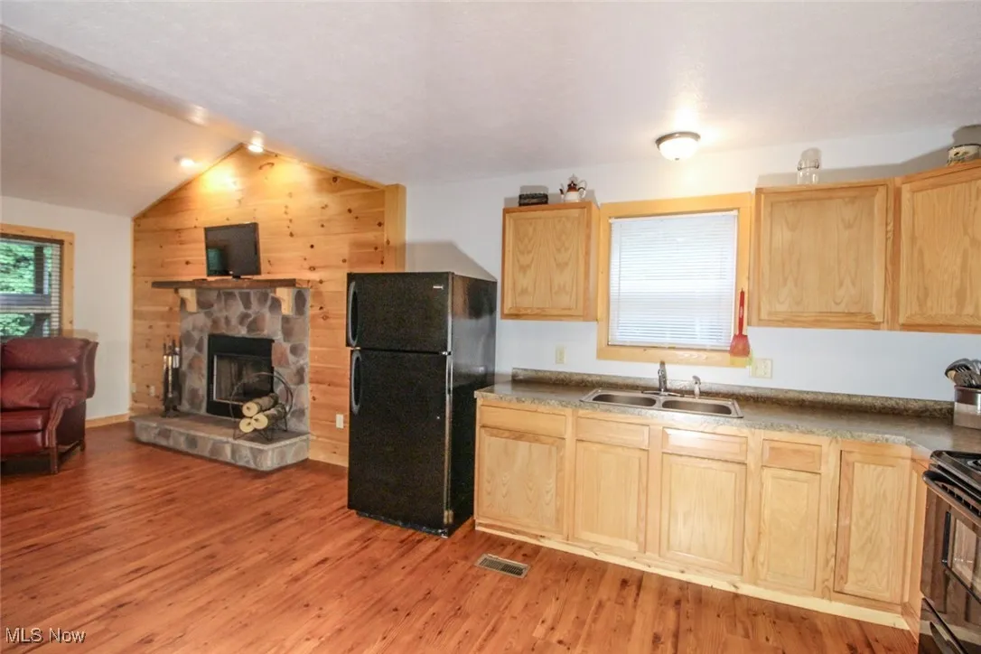 Kitchen featuring light brown cabinets, black appliances, light wood-type flooring, vaulted ceiling, and wood walls