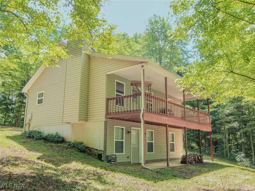Rear view of house featuring a chimney, a patio, a wooden deck, and a yard
