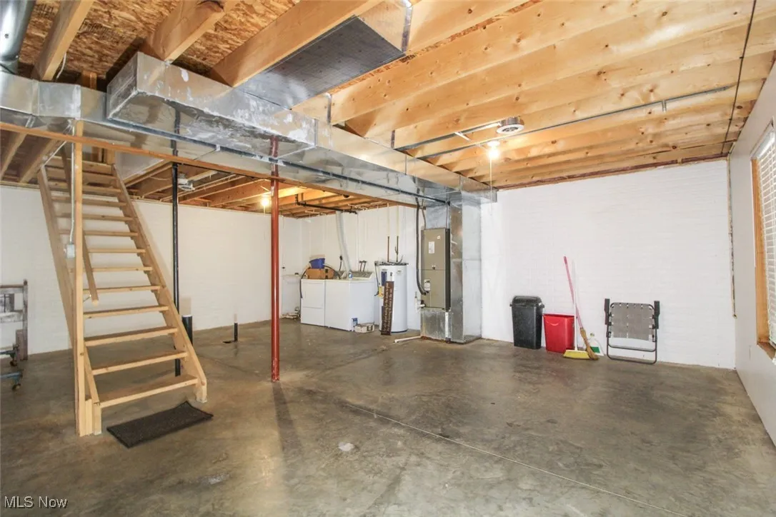 Unfinished below grade area with washer and dryer, heating unit, stairway, gas water heater, and brick wall