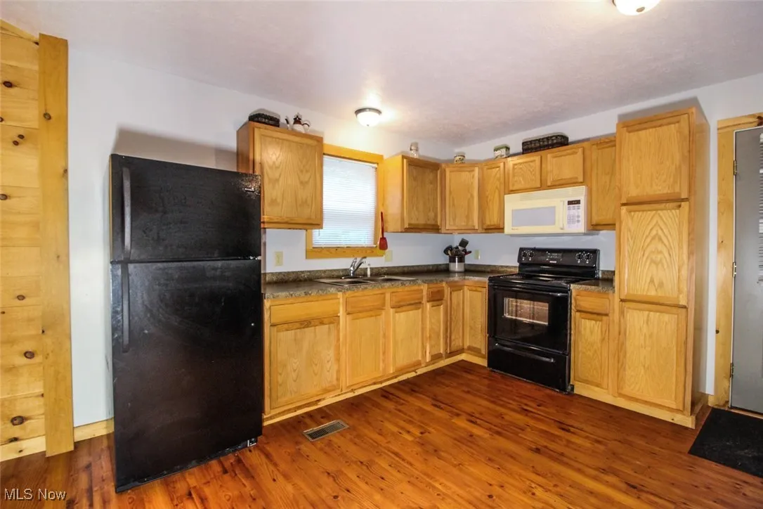 Kitchen with black appliances, dark countertops, and dark wood finished floors