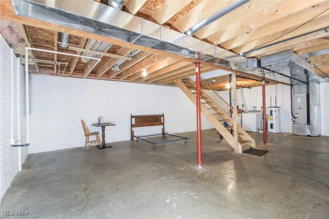 Unfinished below grade area featuring heating unit, water heater, washing machine and clothes dryer, and stairs