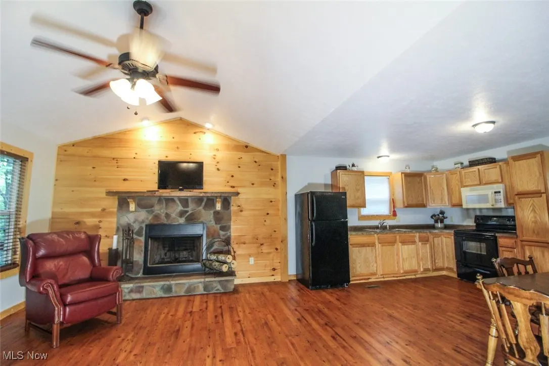 Kitchen with lofted ceiling, black appliances, dark countertops, dark wood finished floors, and wood walls