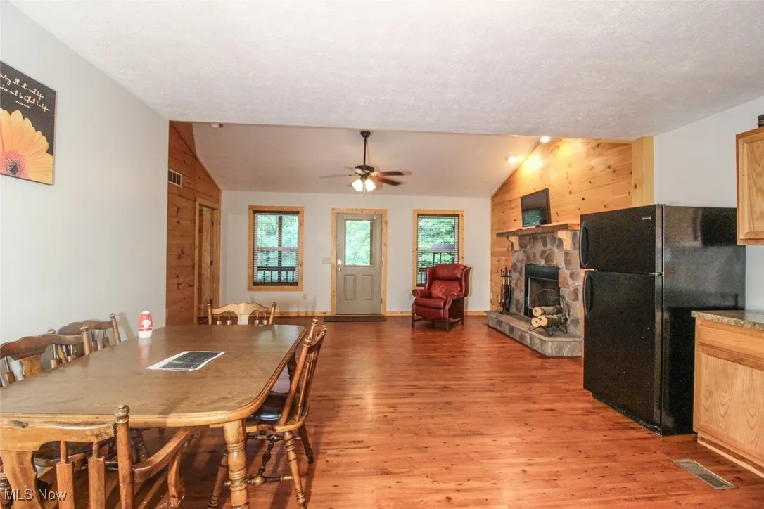 Dining area featuring light wood finished floors, lofted ceiling, a fireplace, ceiling fan, and a textured ceiling