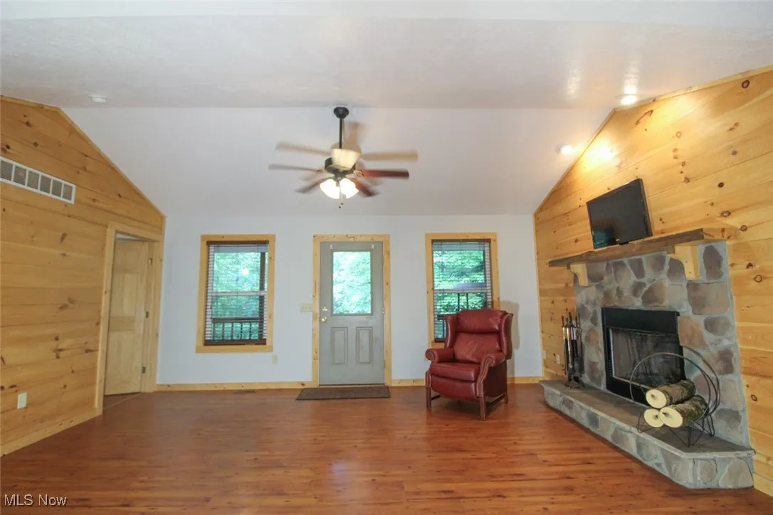 Living room with wood walls, lofted ceiling, wood finished floors, a fireplace, and ceiling fan