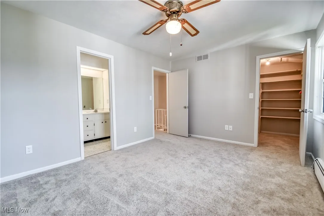 Unfurnished bedroom featuring a walk in closet, carpet, ensuite bathroom, and a baseboard heating unit