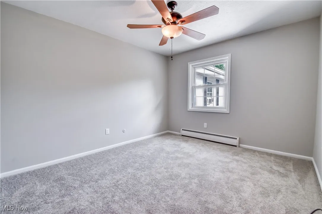 Carpeted spare room featuring a baseboard radiator and ceiling fan