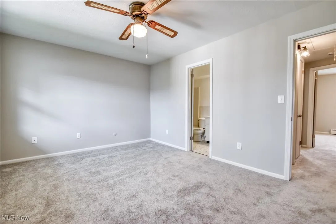 Unfurnished bedroom featuring carpet floors, attic access, ensuite bathroom, and a ceiling fan