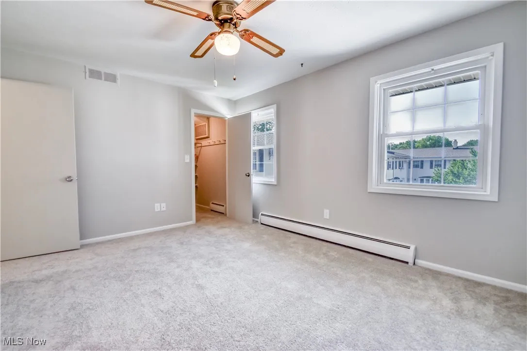 Unfurnished bedroom with baseboard heating, carpet, a baseboard heating unit, and a ceiling fan