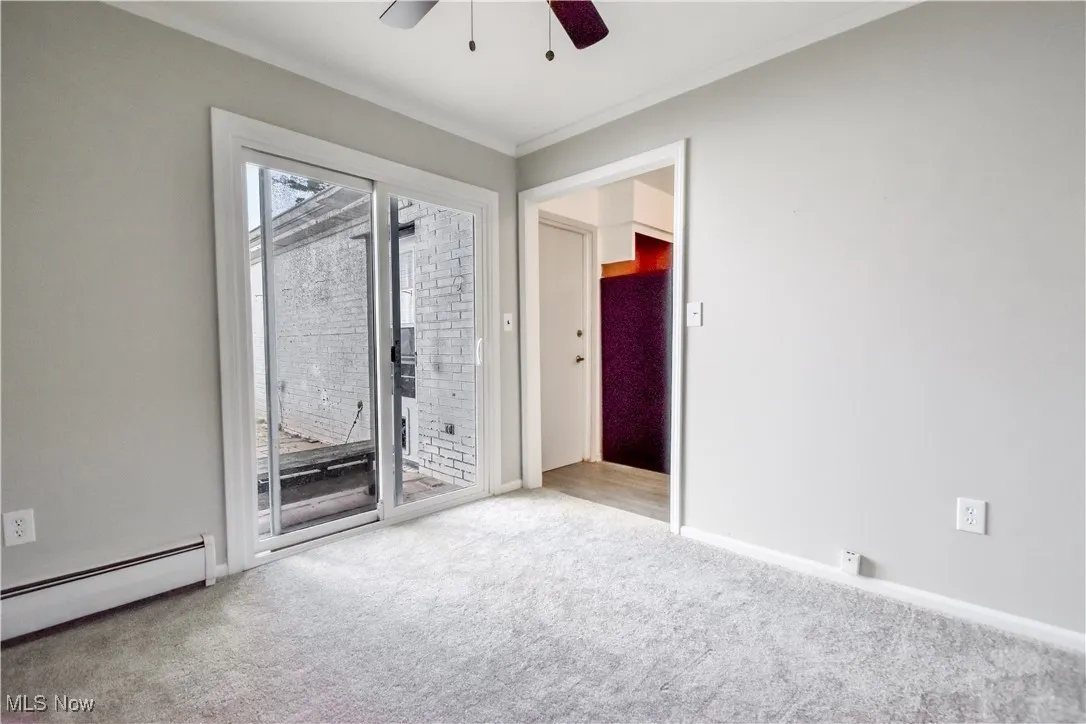 Unfurnished room featuring a baseboard heating unit, a ceiling fan, ornamental molding, and carpet flooring