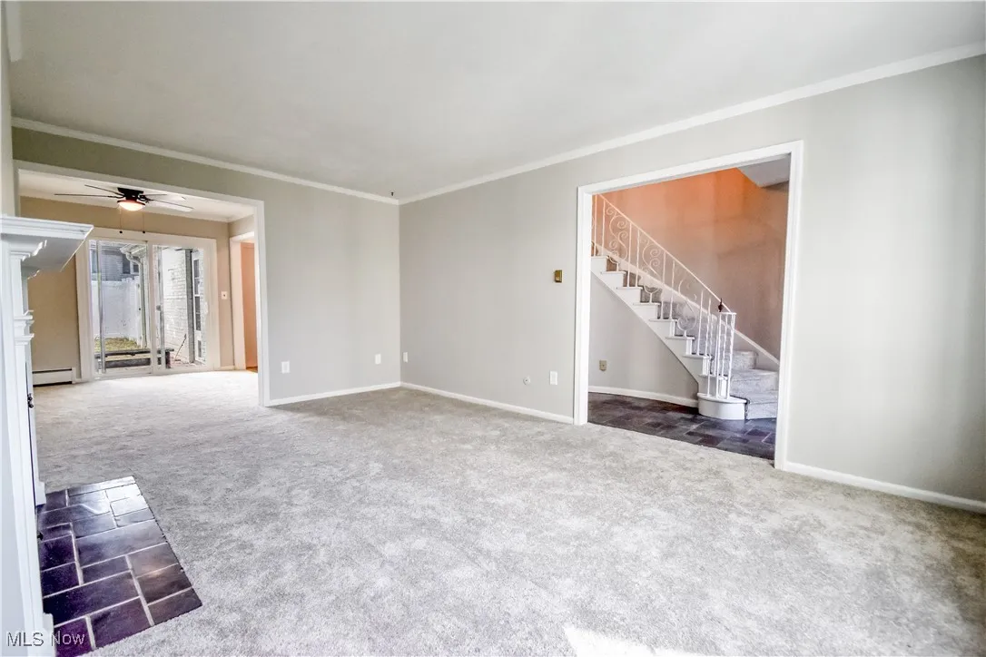 Unfurnished living room featuring carpet flooring, crown molding, stairs, ceiling fan, and baseboard heating