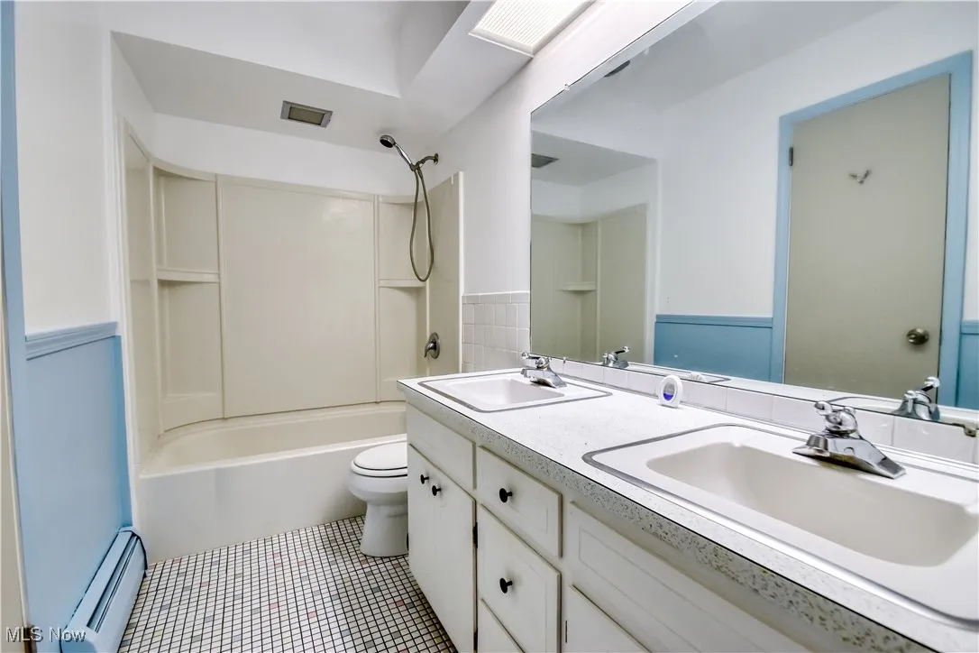 Full bath featuring baseboard heating, double vanity, shower / bathtub combination, tile patterned flooring, and a wainscoted wall