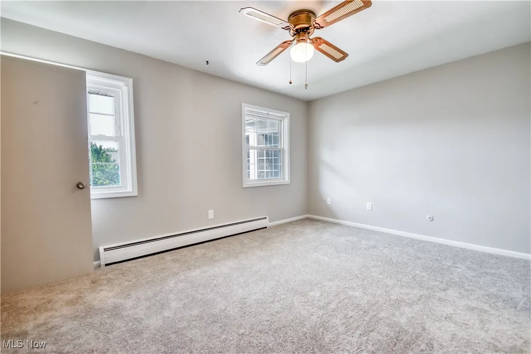 Empty room featuring plenty of natural light, a baseboard radiator, and carpet floors