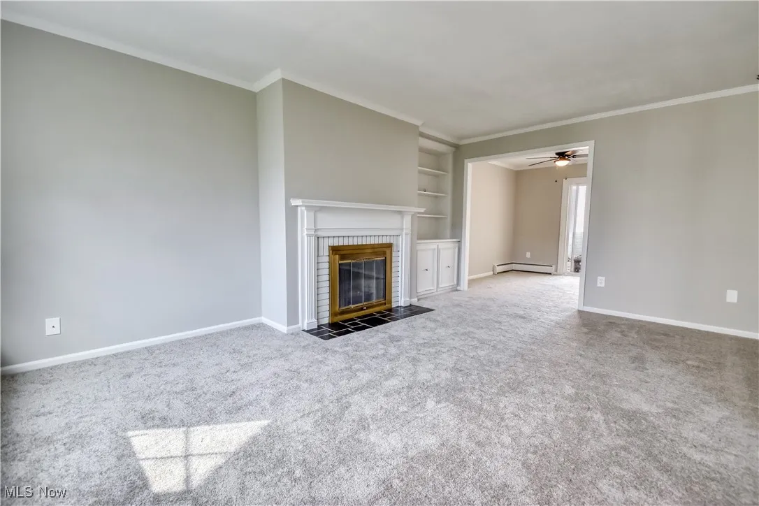 Unfurnished living room featuring built in features, carpet flooring, ceiling fan, a fireplace, and ornamental molding