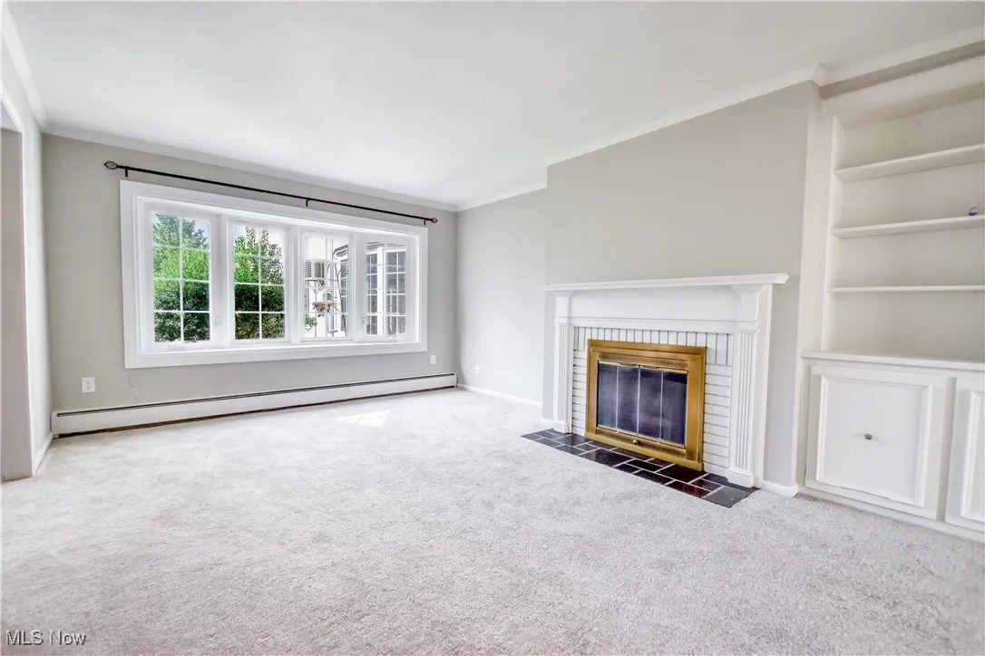 Unfurnished living room with built in shelves, ornamental molding, carpet floors, baseboard heating, and a fireplace