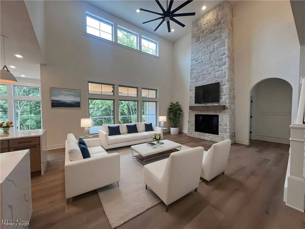 Living room with light wood-type flooring, a fireplace, arched walkways, recessed lighting, and ceiling fan