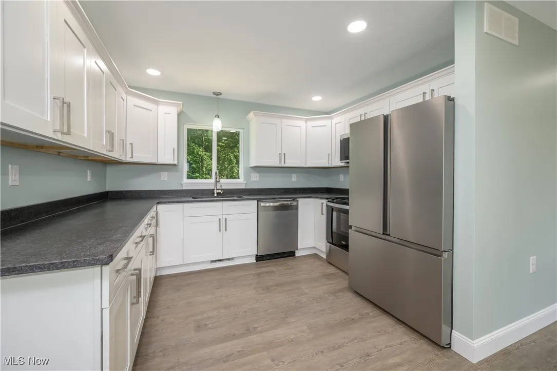 Kitchen featuring stainless steel appliances, dark countertops, light wood-style floors, white cabinets, and hanging light fixtures