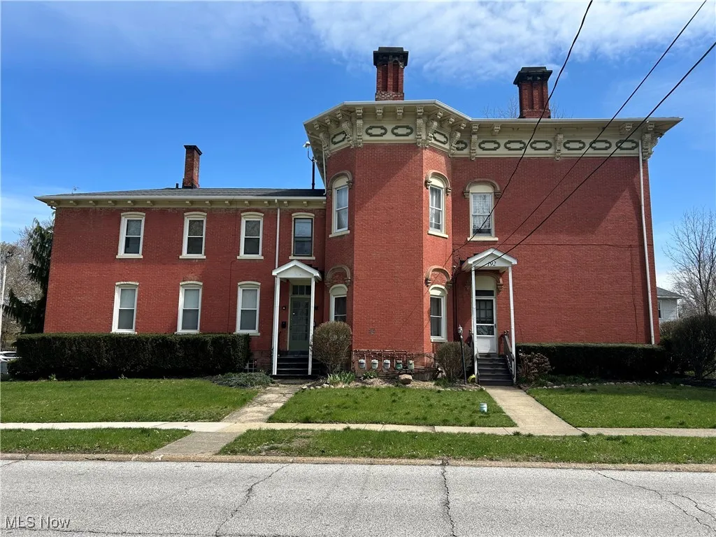 Italianate house with a chimney, a front yard, and brick siding