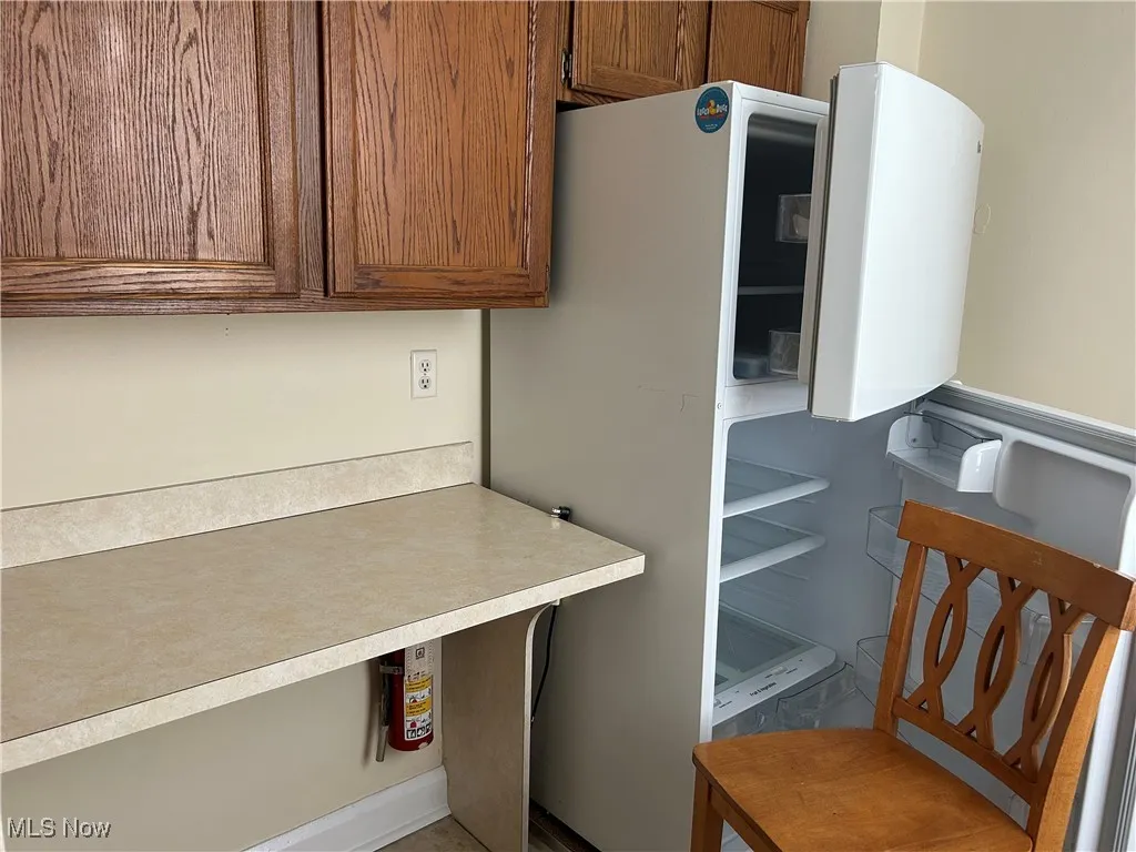 Kitchen featuring freestanding refrigerator, brown cabinetry, and light countertops