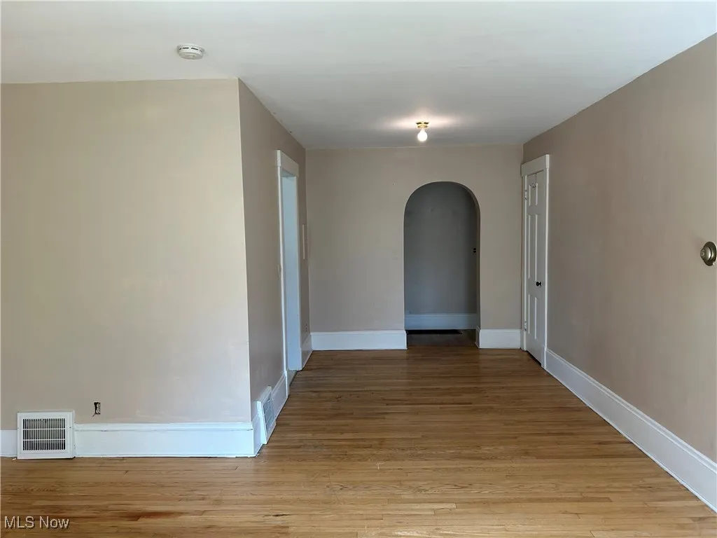 Spare room featuring arched walkways and light wood-style floors