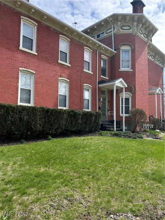 Italianate-style house with brick siding, a front lawn, and a chimney