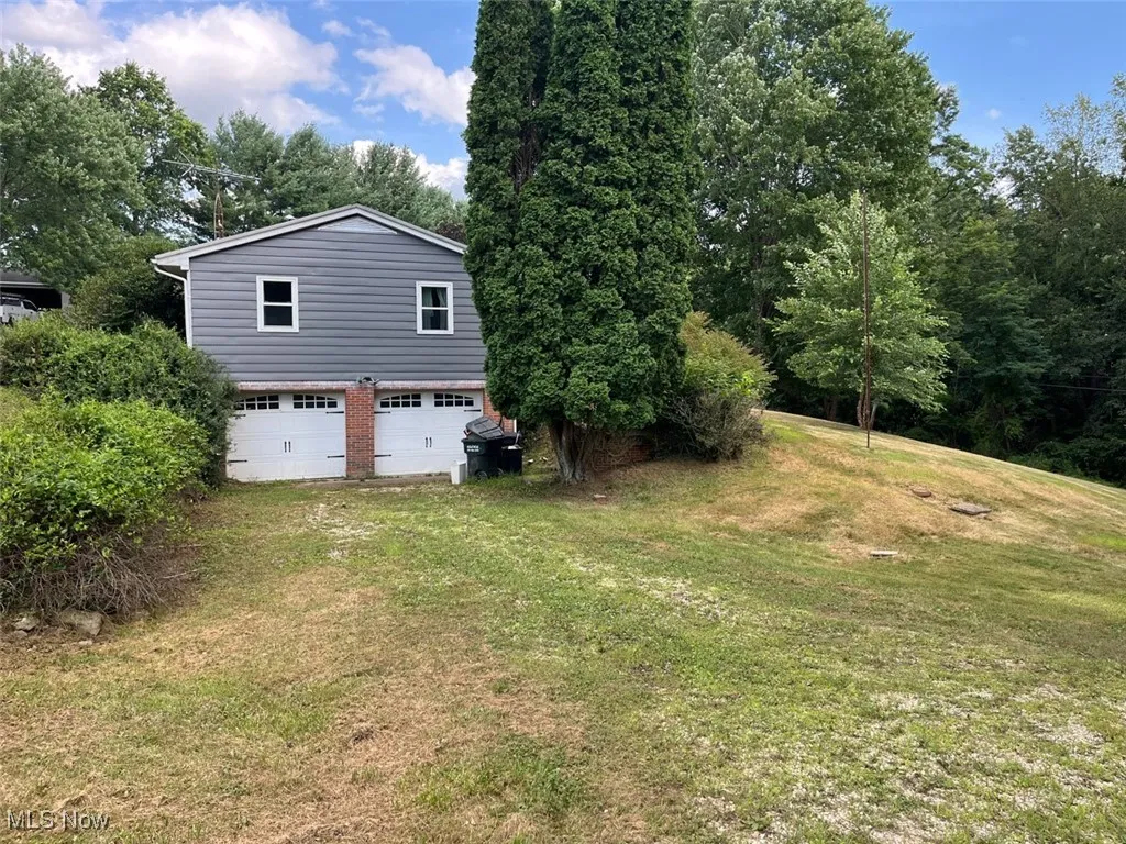 View of property exterior with a garage, a yard, and driveway