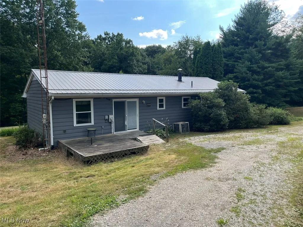 Rear view of property featuring a metal roof, a deck, a view of trees, and a yard