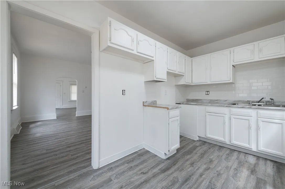 Kitchen featuring arched walkways, white cabinets, decorative backsplash, and light wood finished floors