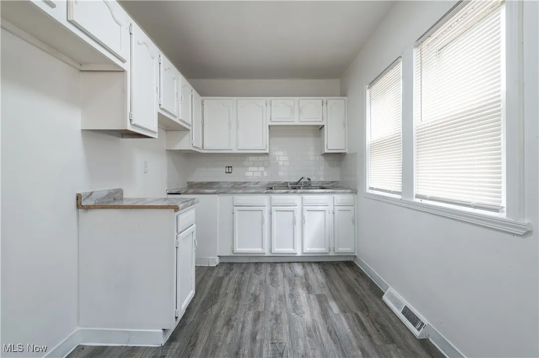 Kitchen featuring tasteful backsplash, white cabinetry, wood finished floors, and light countertops