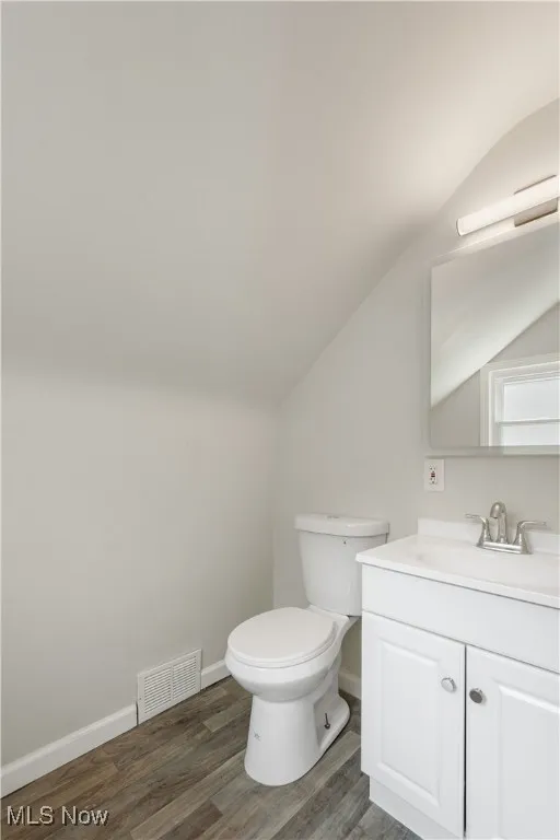 Half bath with vanity, wood finished floors, and vaulted ceiling