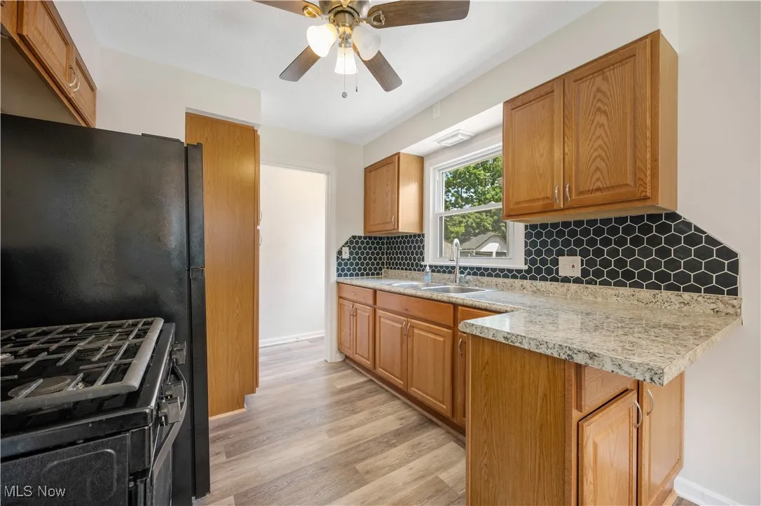 Kitchen with stainless steel range with gas stovetop, backsplash, light wood finished floors, light countertops, and ceiling fan