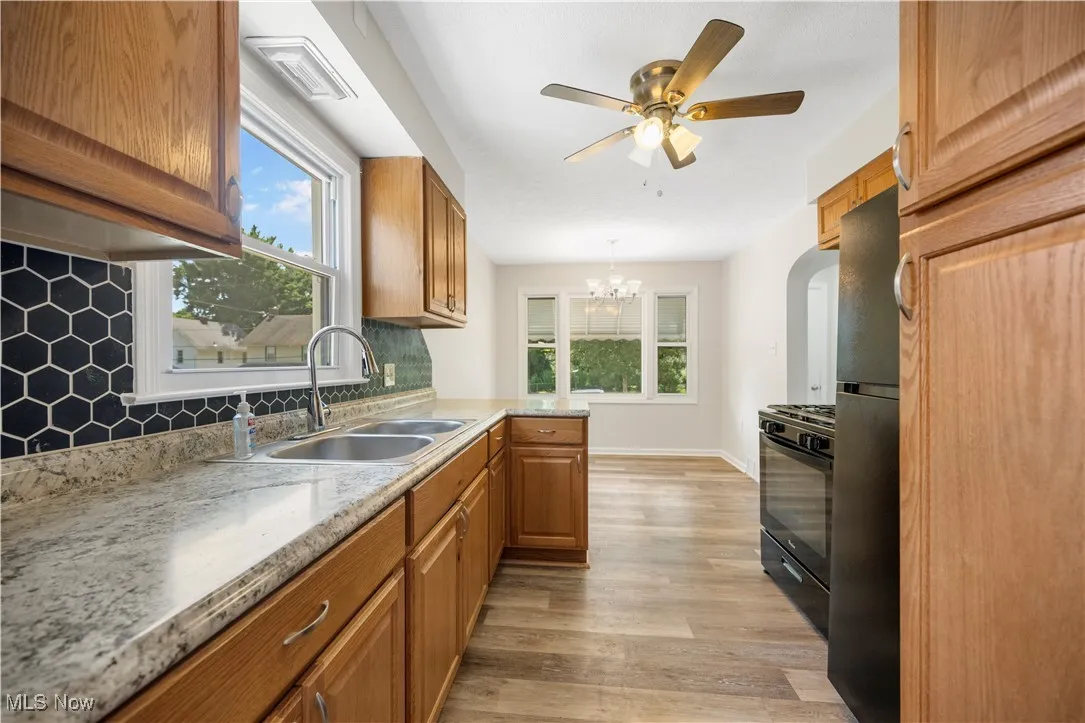 Kitchen featuring freestanding refrigerator, decorative backsplash, black gas stove, light wood-style floors, and brown cabinetry