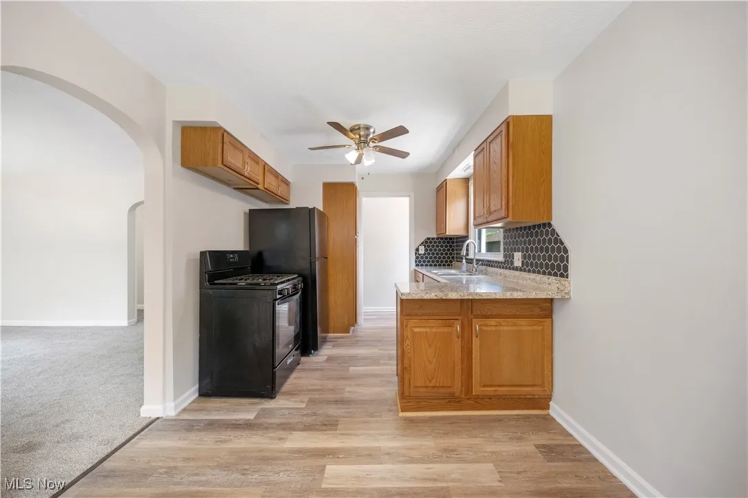 Kitchen featuring black gas stove, a ceiling fan, backsplash, arched walkways, and brown cabinetry