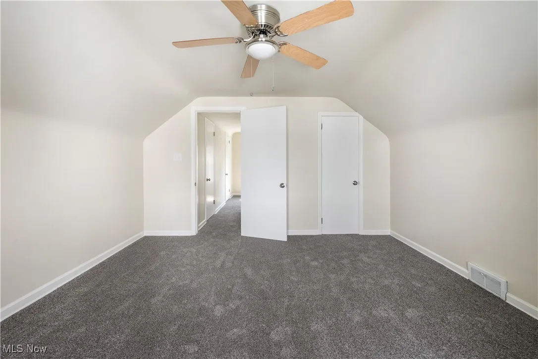 Additional living space with dark carpet, lofted ceiling, and a ceiling fan