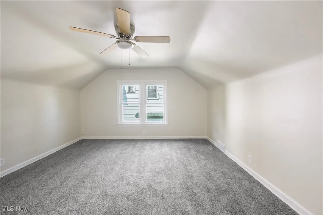 Additional living space featuring carpet flooring, vaulted ceiling, and a ceiling fan