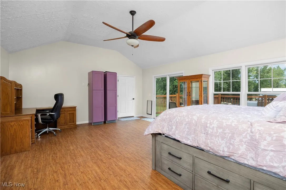 Bedroom with vaulted ceiling, a desk, light wood finished floors, access to exterior, and a textured ceiling
