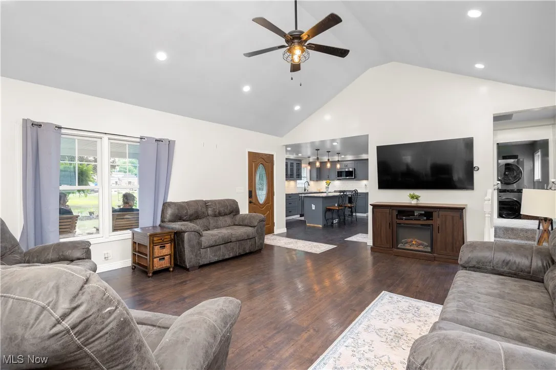 Living room with stacked washer and clothes dryer, recessed lighting, a ceiling fan, dark wood-type flooring, and high vaulted ceiling