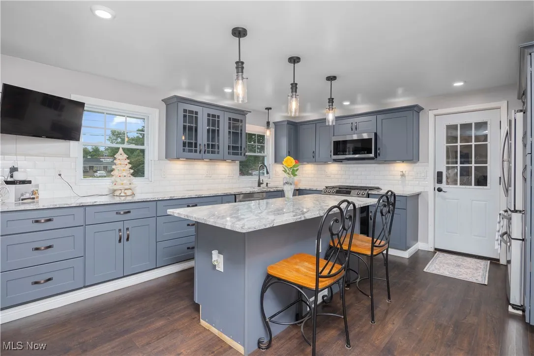 Kitchen with recessed lighting, dark wood-style flooring, appliances with stainless steel finishes, light stone counters, and a kitchen bar