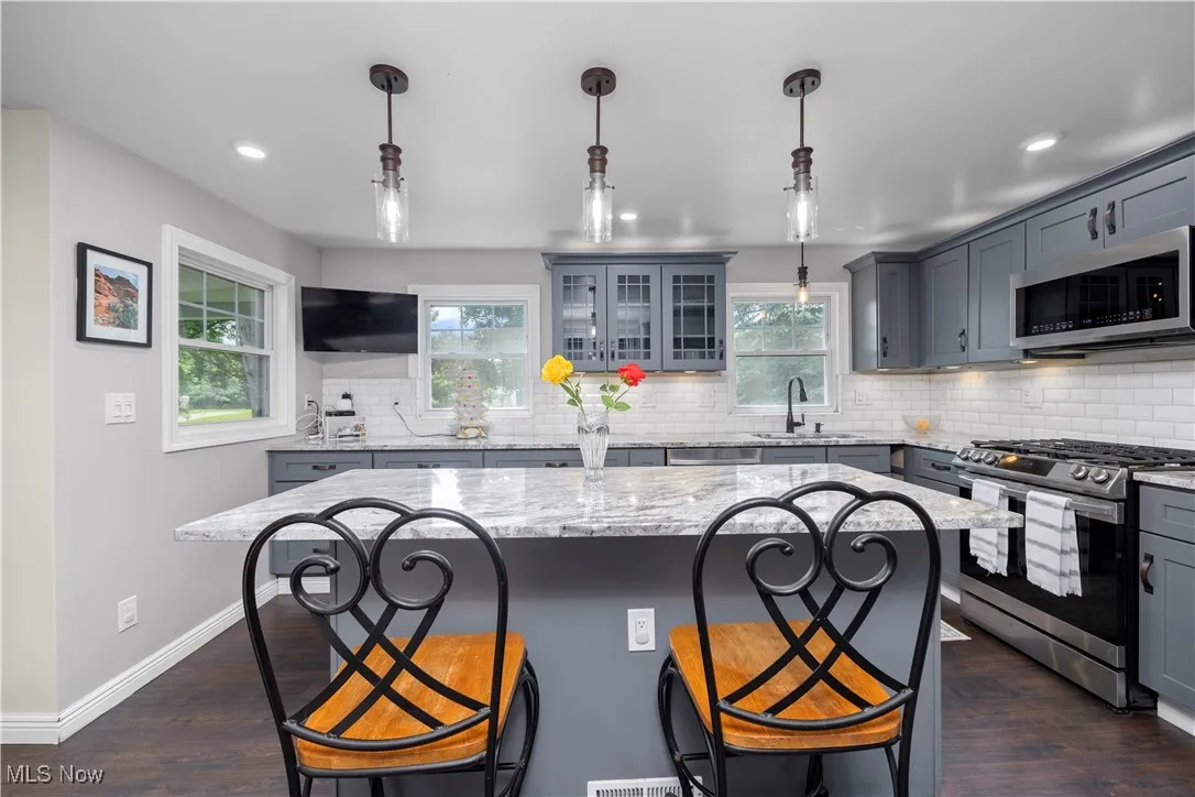 Kitchen featuring appliances with stainless steel finishes, gray cabinets, a kitchen bar, dark wood-type flooring, and light stone counters