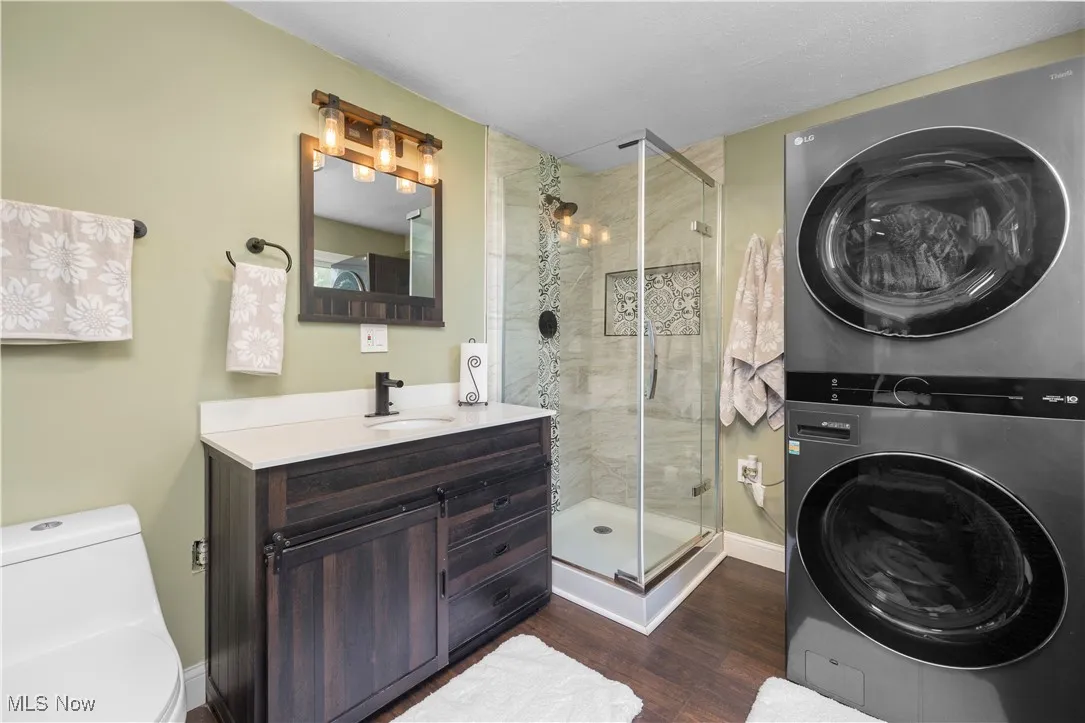 Bathroom with estacked washer and dryer, a stall shower, vanity, and wood finished floors