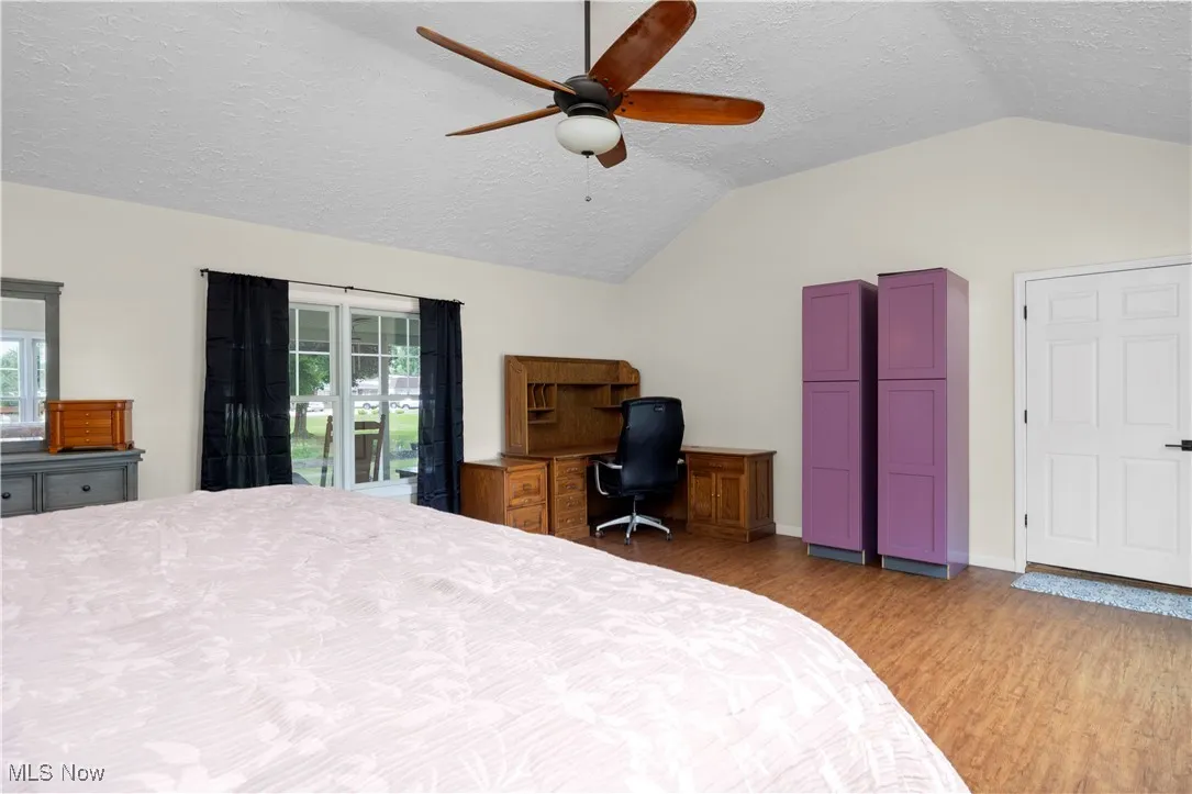 Bedroom with a textured ceiling, light wood-type flooring, vaulted ceiling, an office area, and a ceiling fan