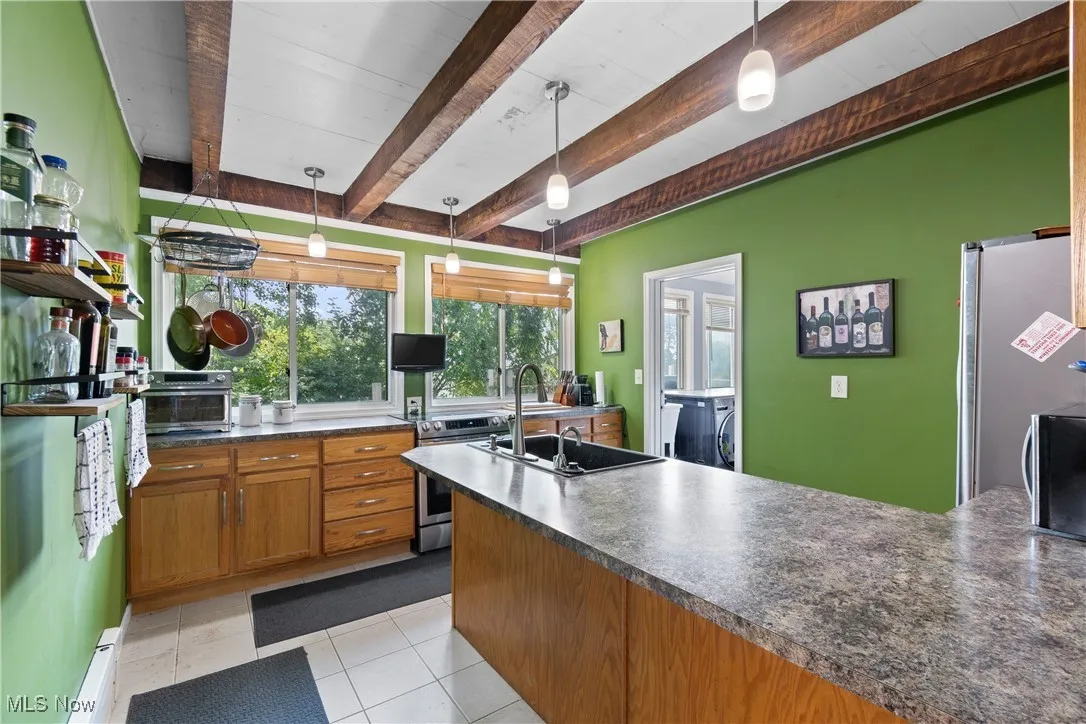 Kitchen featuring dark countertops, beamed ceiling, stainless steel appliances, baseboard heating, and decorative light fixtures