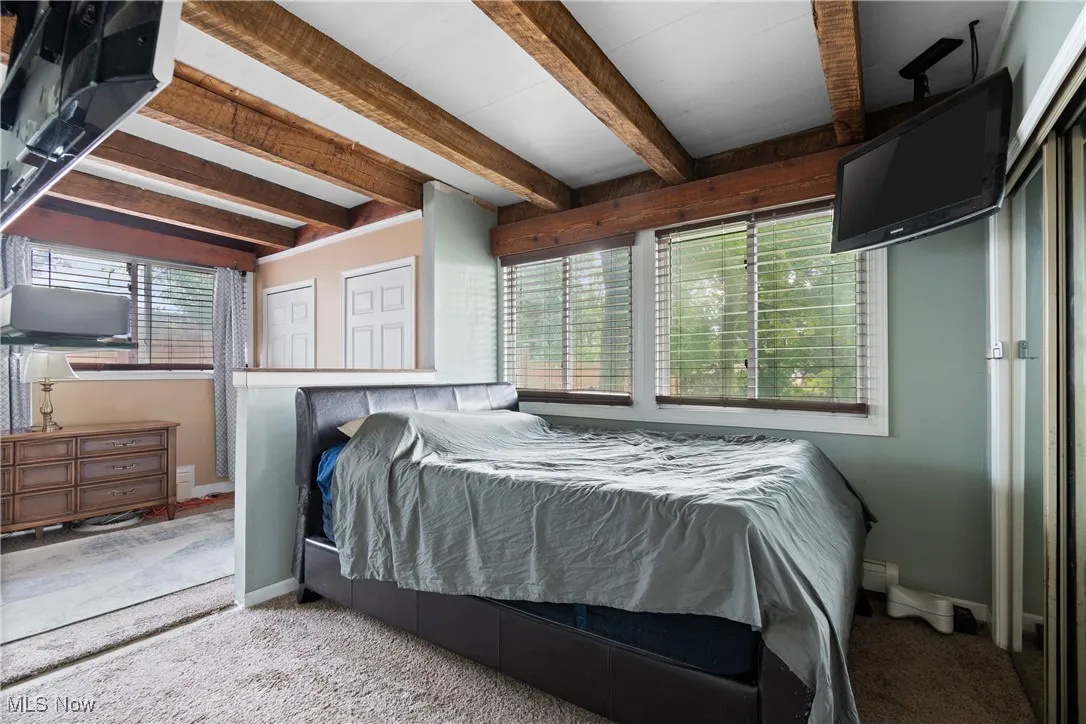 Carpeted bedroom featuring beamed ceiling and multiple windows